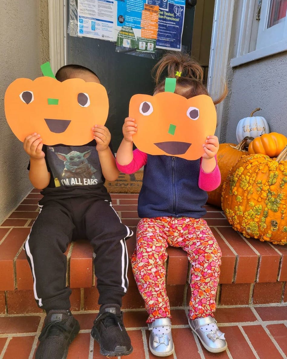 Two children holding up paper pumpkins to cover their faces