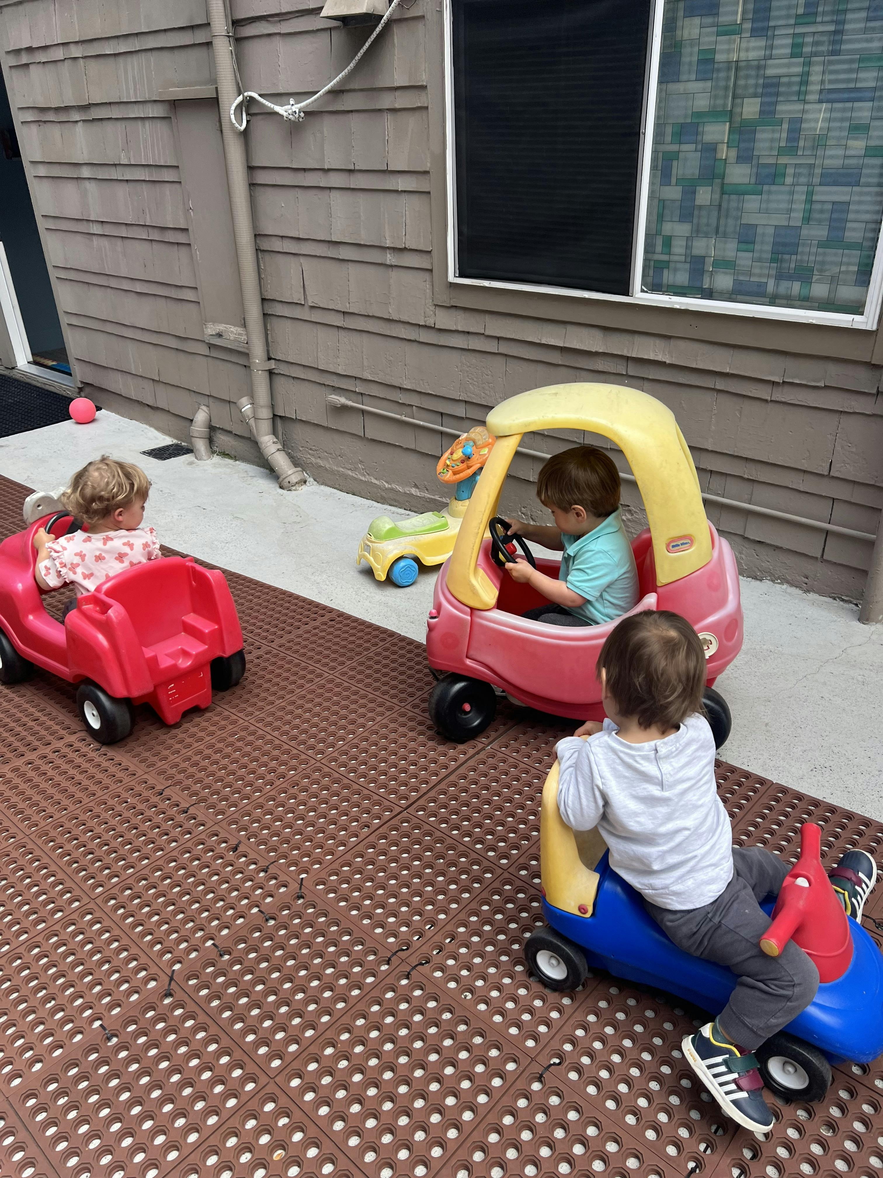 Three children playing with ride-on toys outdoors