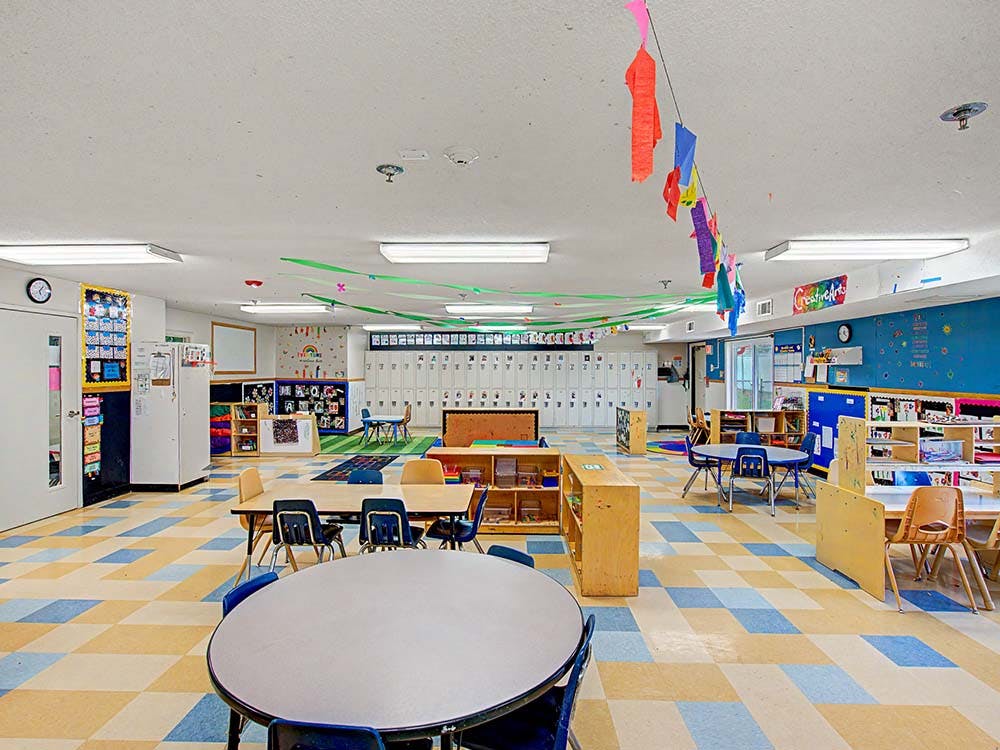 An empty classroom with small tables and chairs, colorful decorations