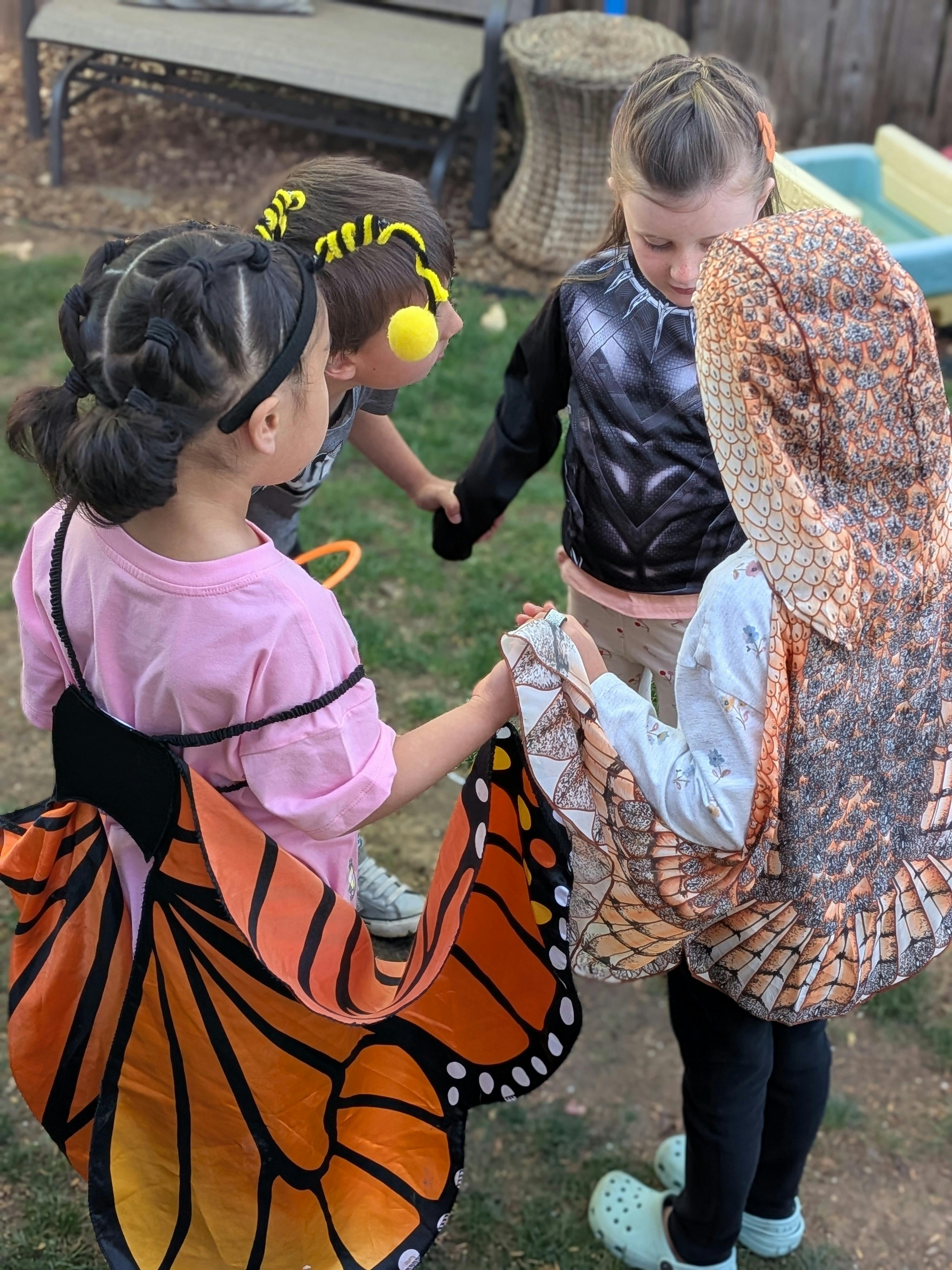 Four children in diverse Halloween costumes holding hands in a circle
