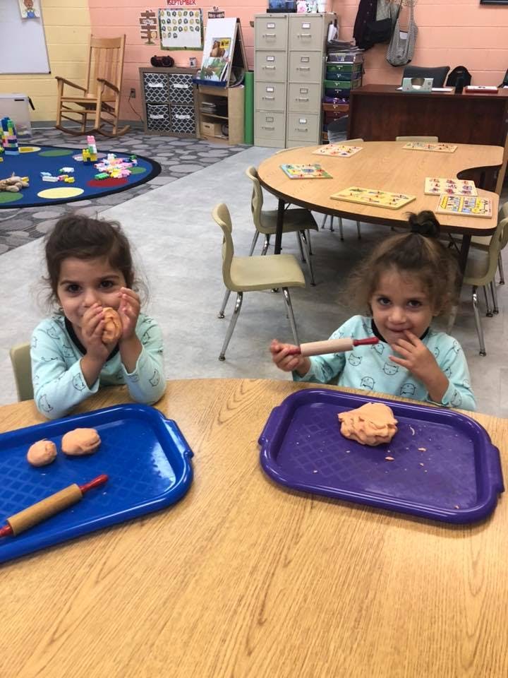 Two children playing with modeling clay at a table in a classroom