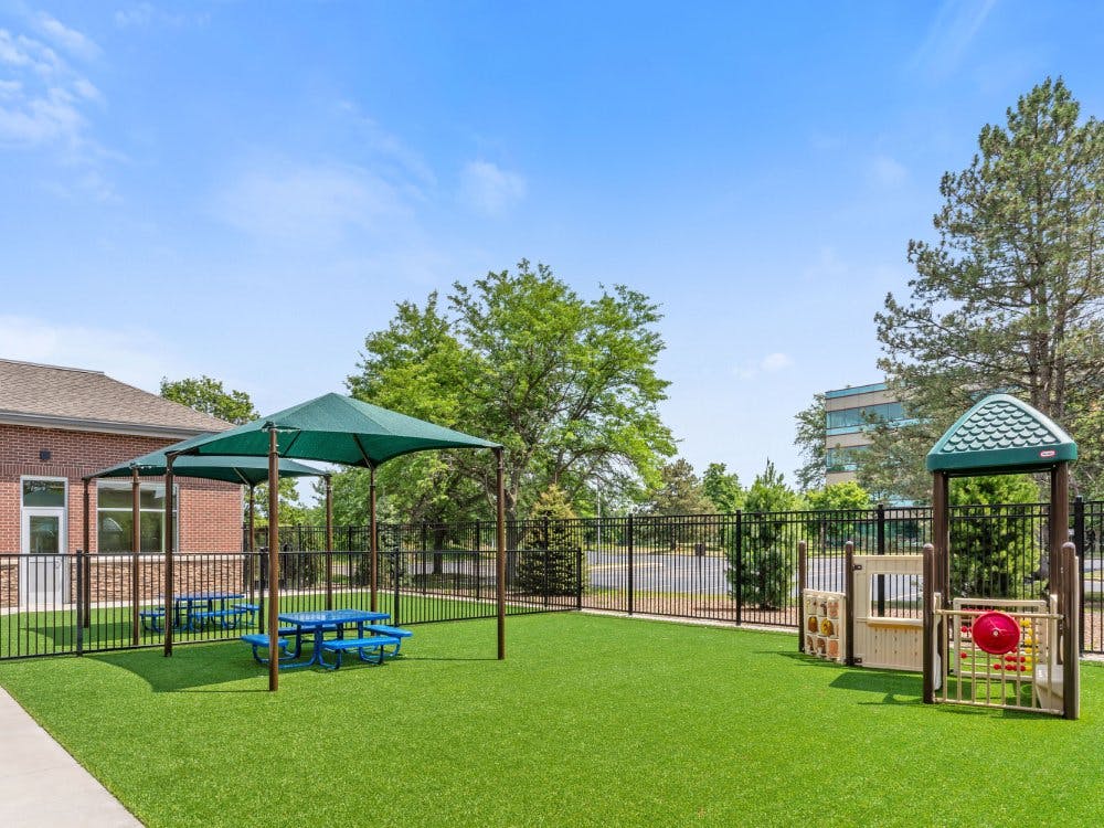 Outdoor play area with picnic tables under shades and a small playground structure