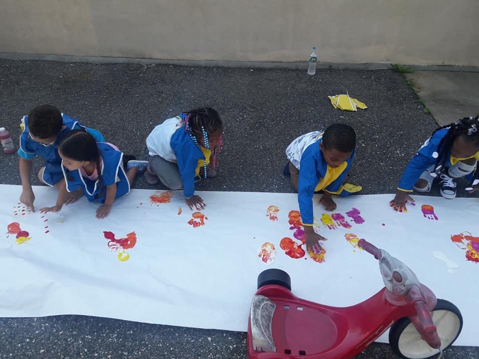 Children kneeling on a large sheet of paper, finger painting