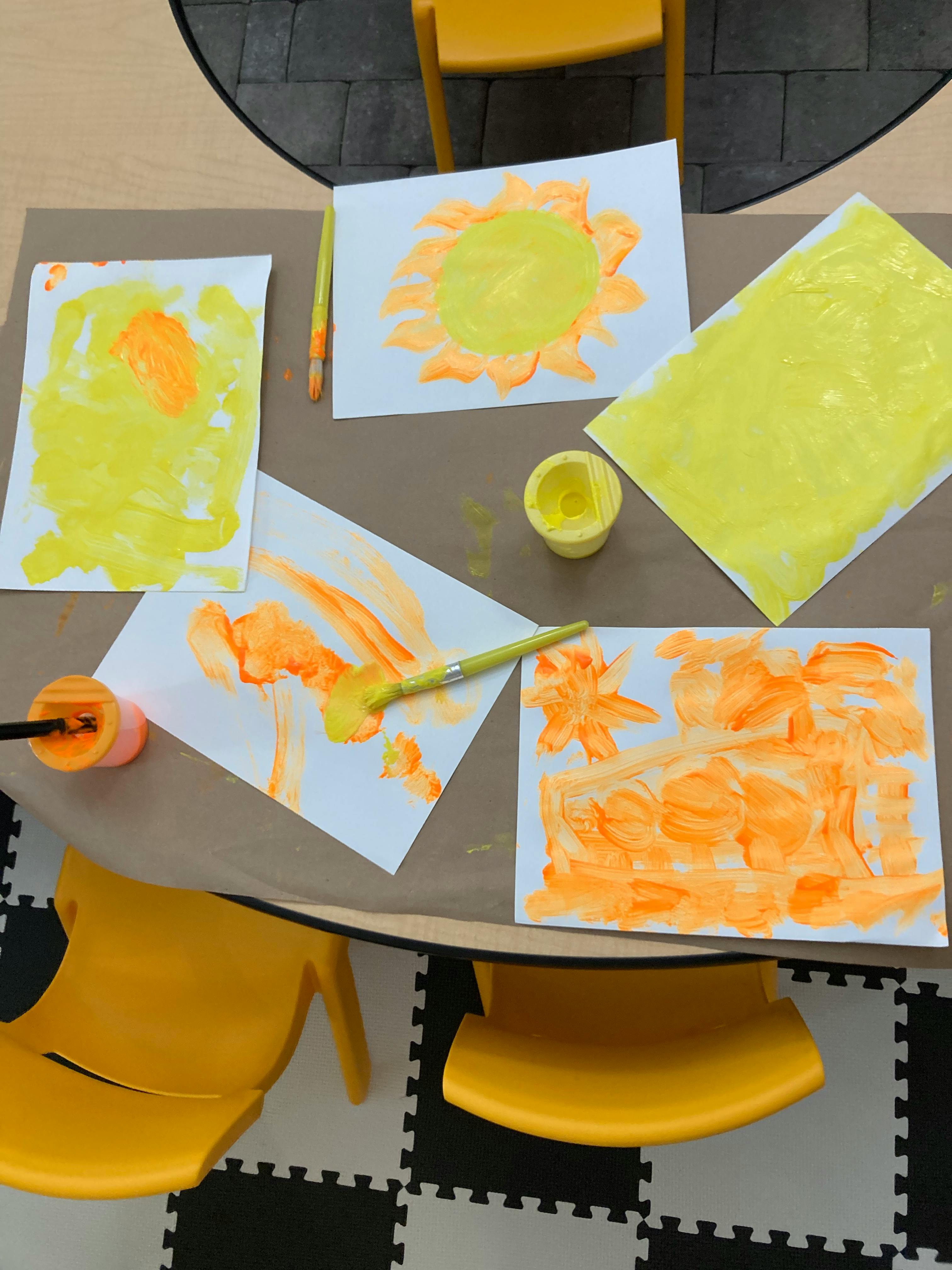 Children's paintings with yellow and orange paint on a table