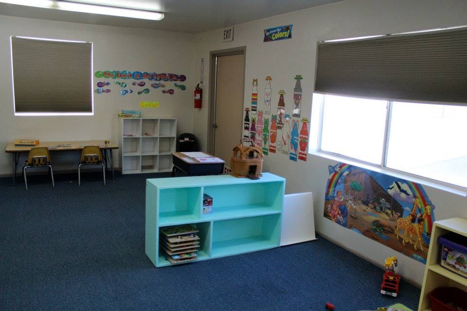 Empty classroom with blue carpet, shelves, tables, and windows