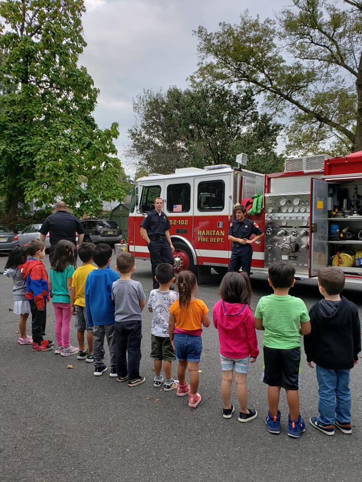 Children in a line facing firefighters and a fire truck