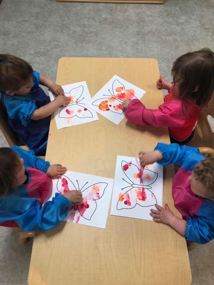 Four children painting butterfly outlines at a table