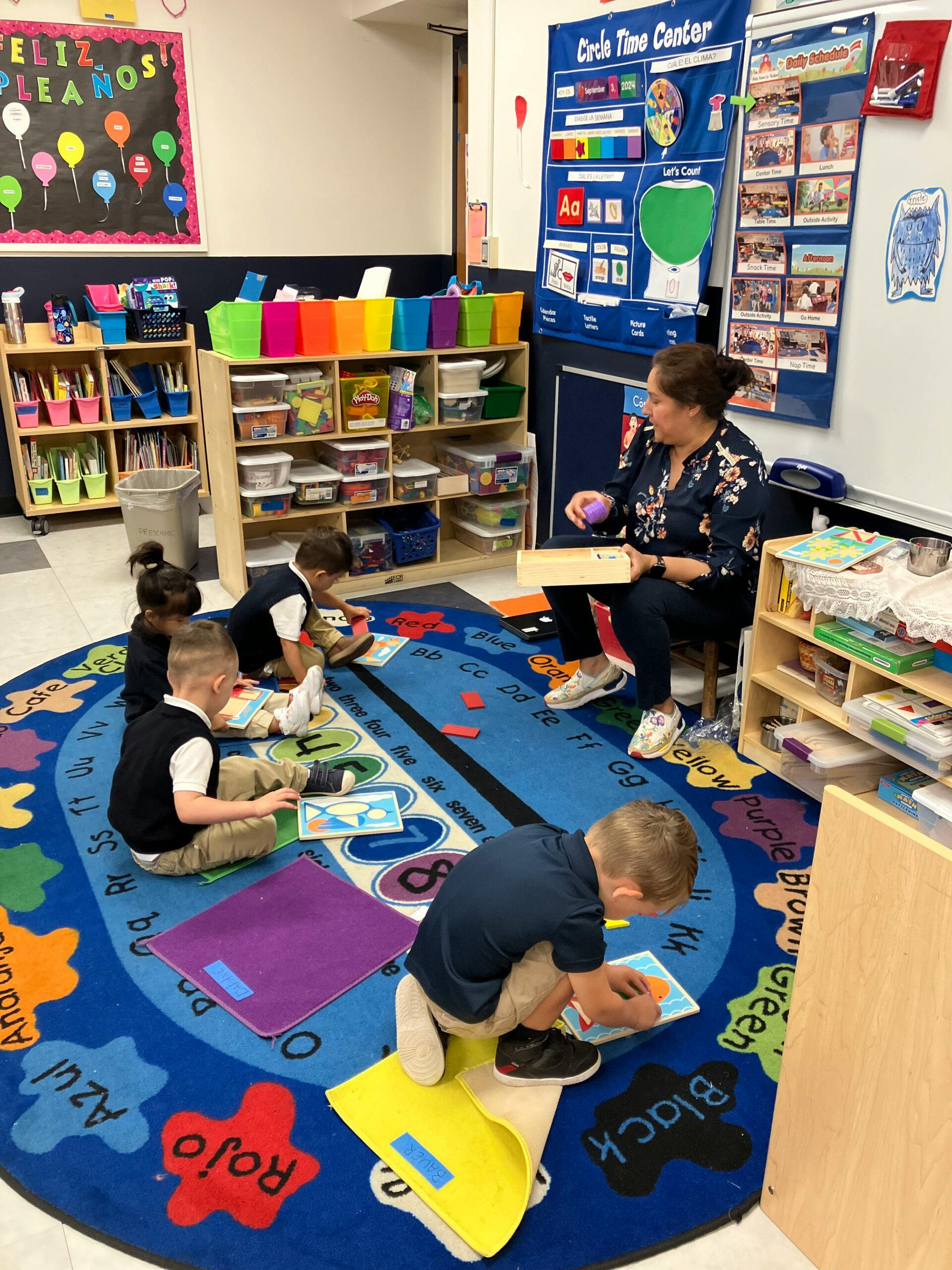 Teacher and children on a colorful rug in a classroom, playing with learning materials