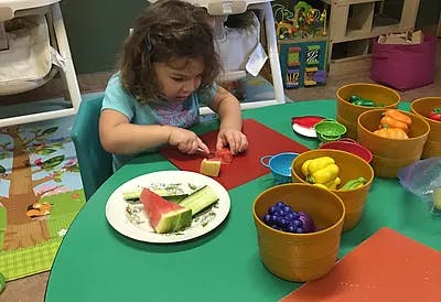 Child cutting food on a red mat at a green table