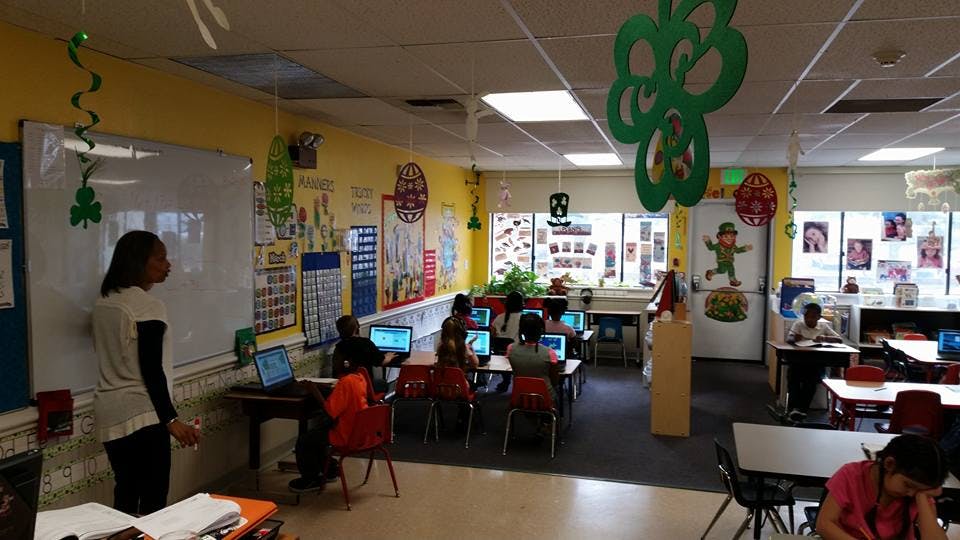 Person standing at whiteboard in classroom with children at computers