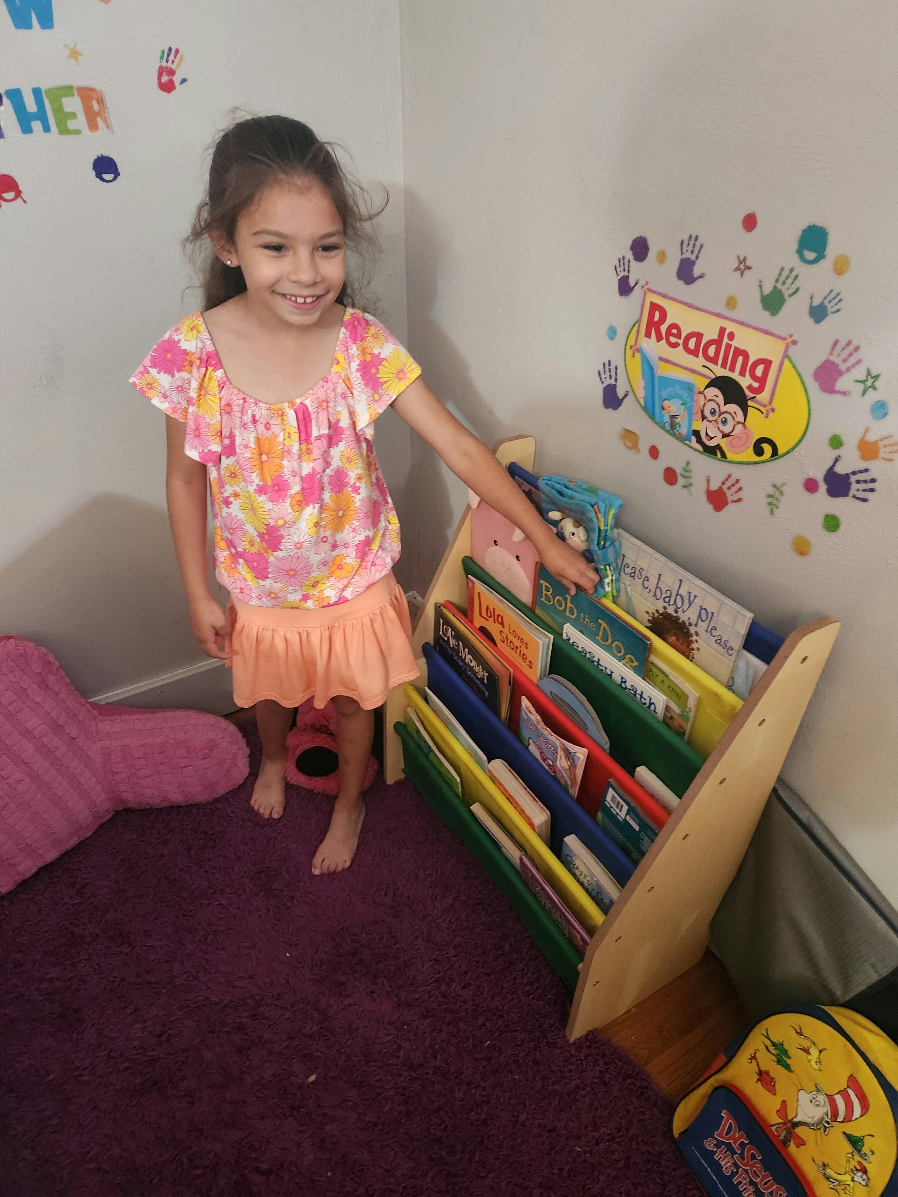 Child standing next to a bookshelf, reaching for a book