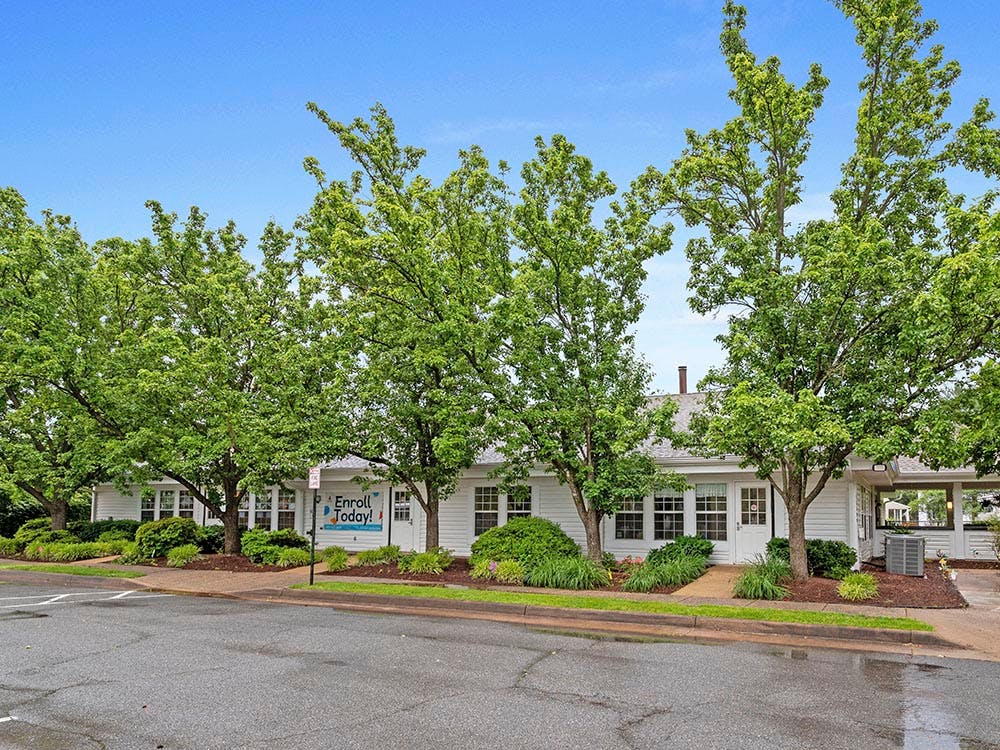 White building with green trees in front, 'Enroll Today!' sign on window