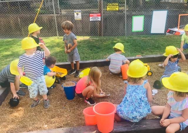 Children in yellow hard hats playing in a sandbox
