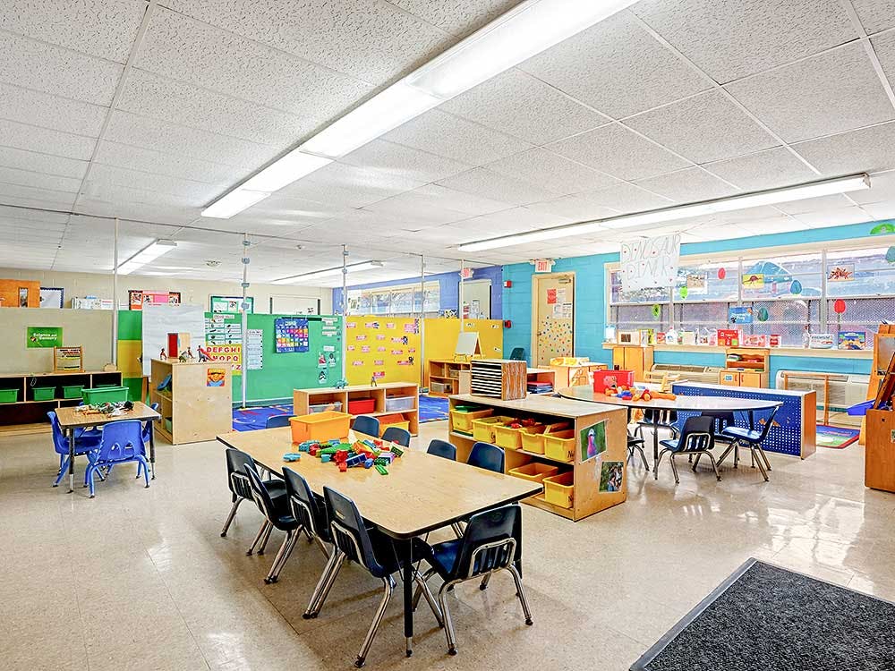 Empty classroom with small tables and chairs, colorful walls, and toys