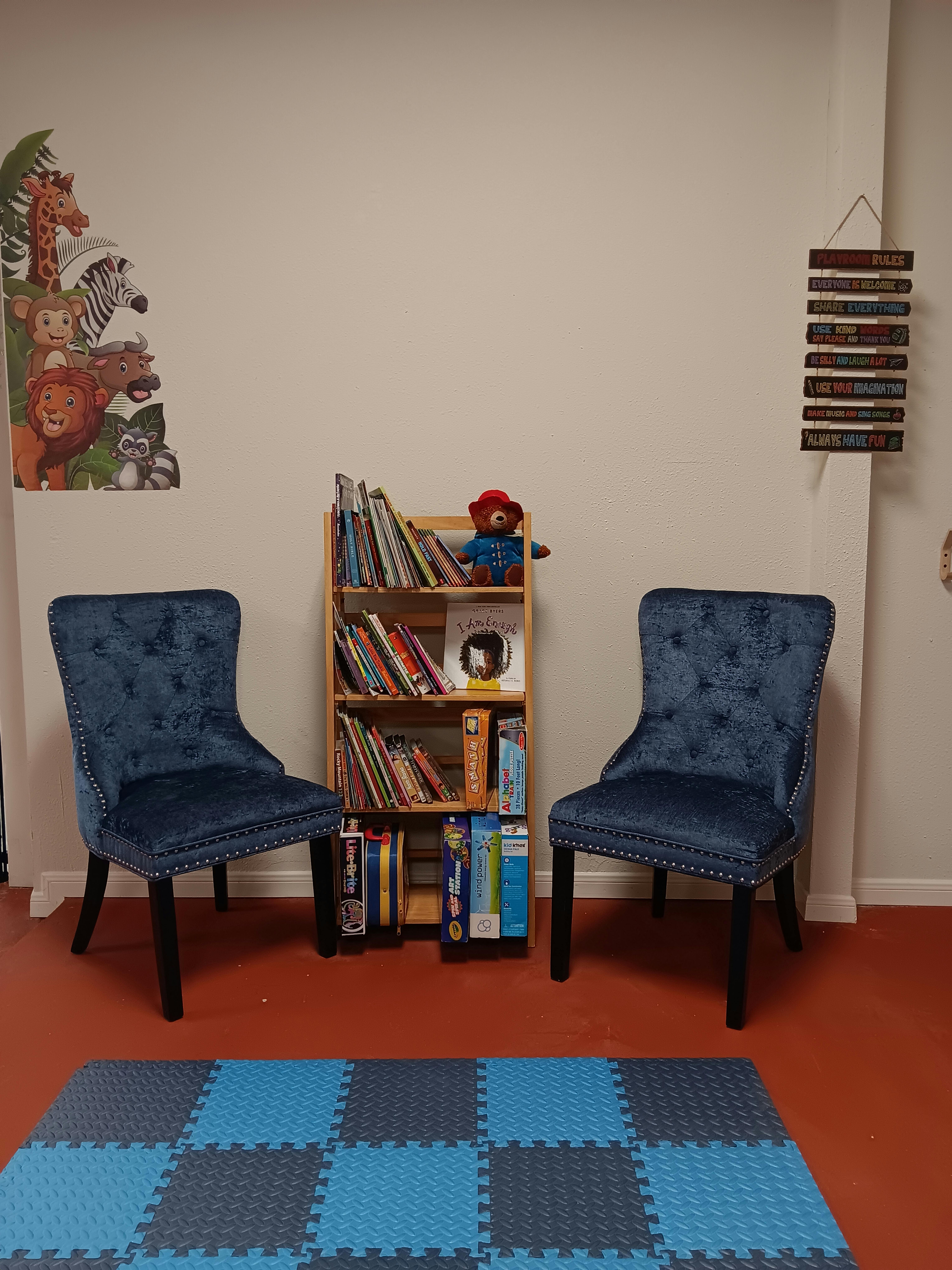 Two blue chairs flanking a bookshelf with books and a teddy bear