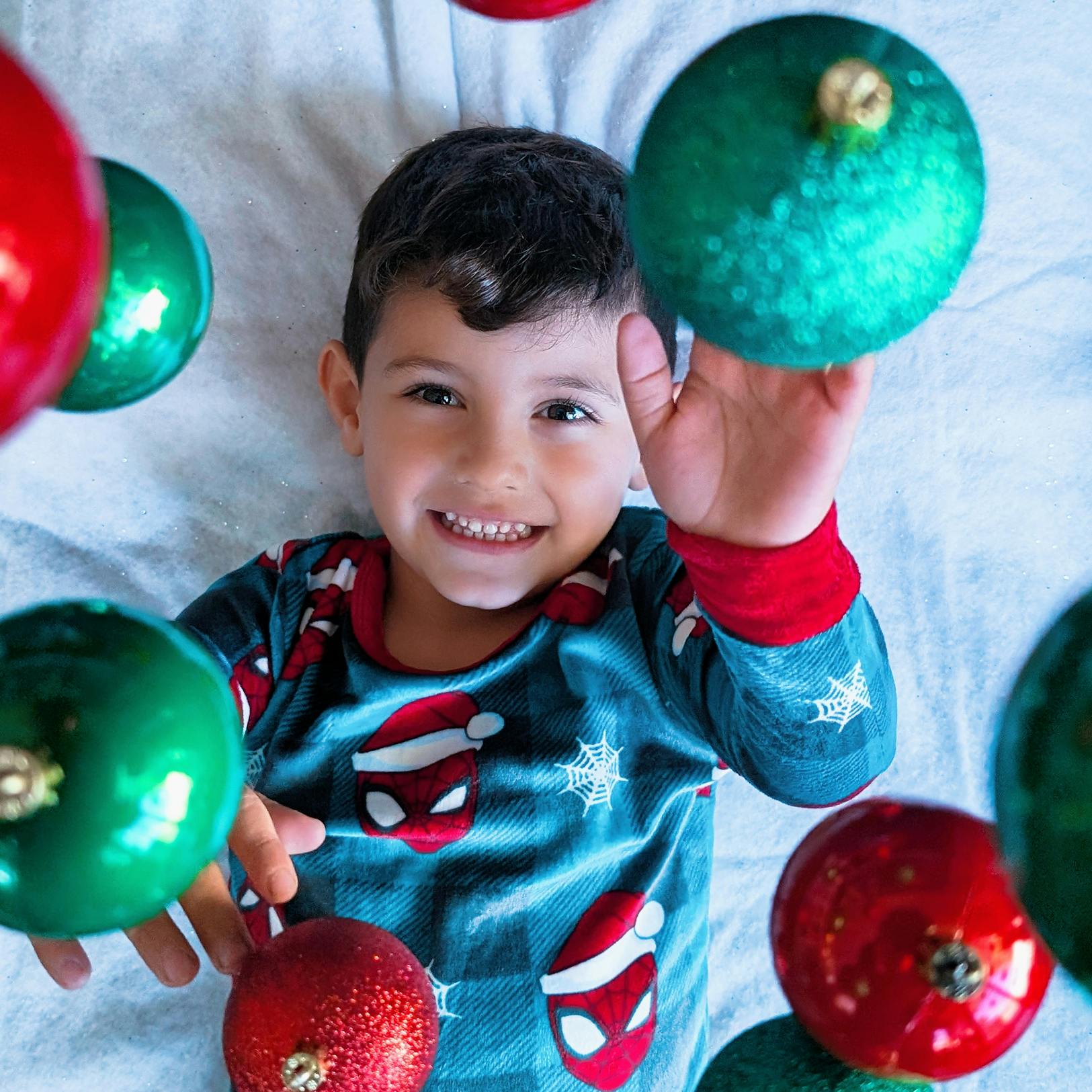 Child lying down surrounded by hanging christmas ornaments