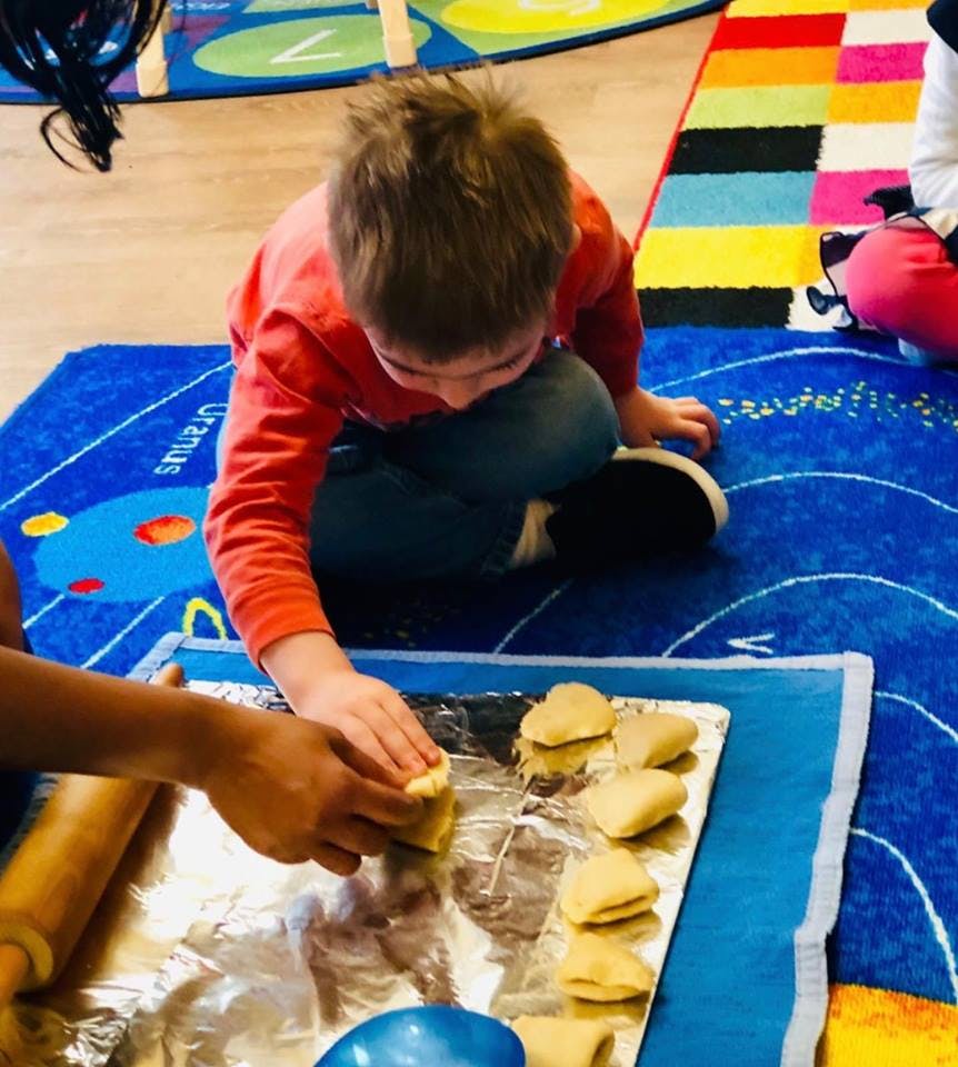 Child on floor placing dough on foil next to a rolling pin