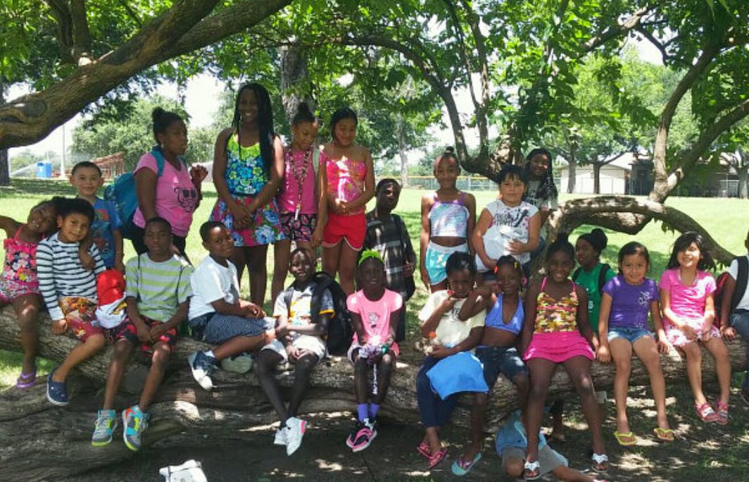 Group of children and teens sitting on a large tree branch outdoors