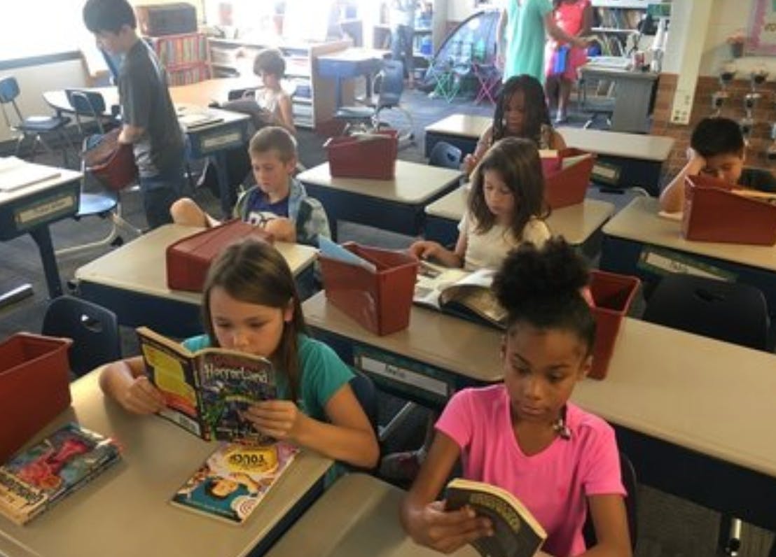 Children reading books at desks in a classroom