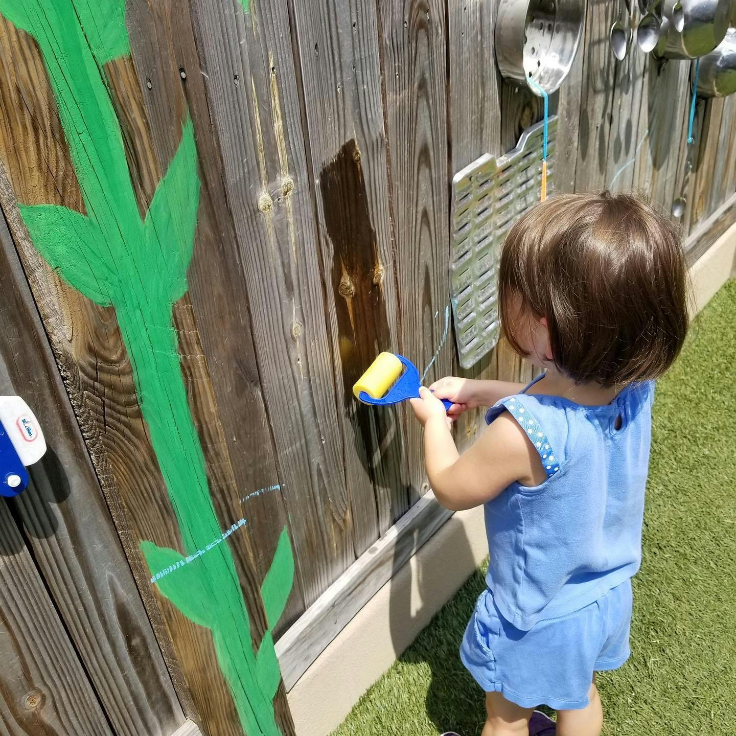 Child painting a wooden fence with a roller