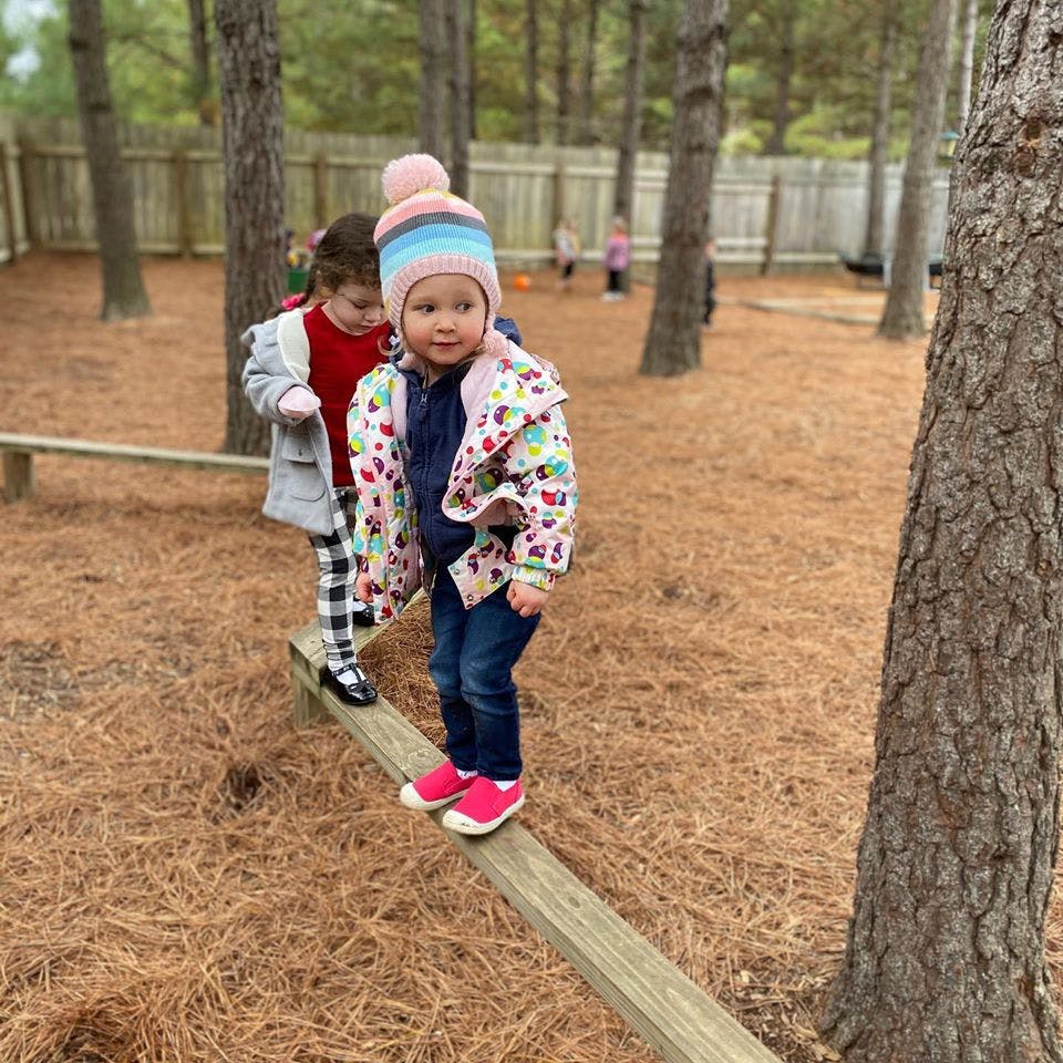 Child in a hat walking on a wooden beam outdoors