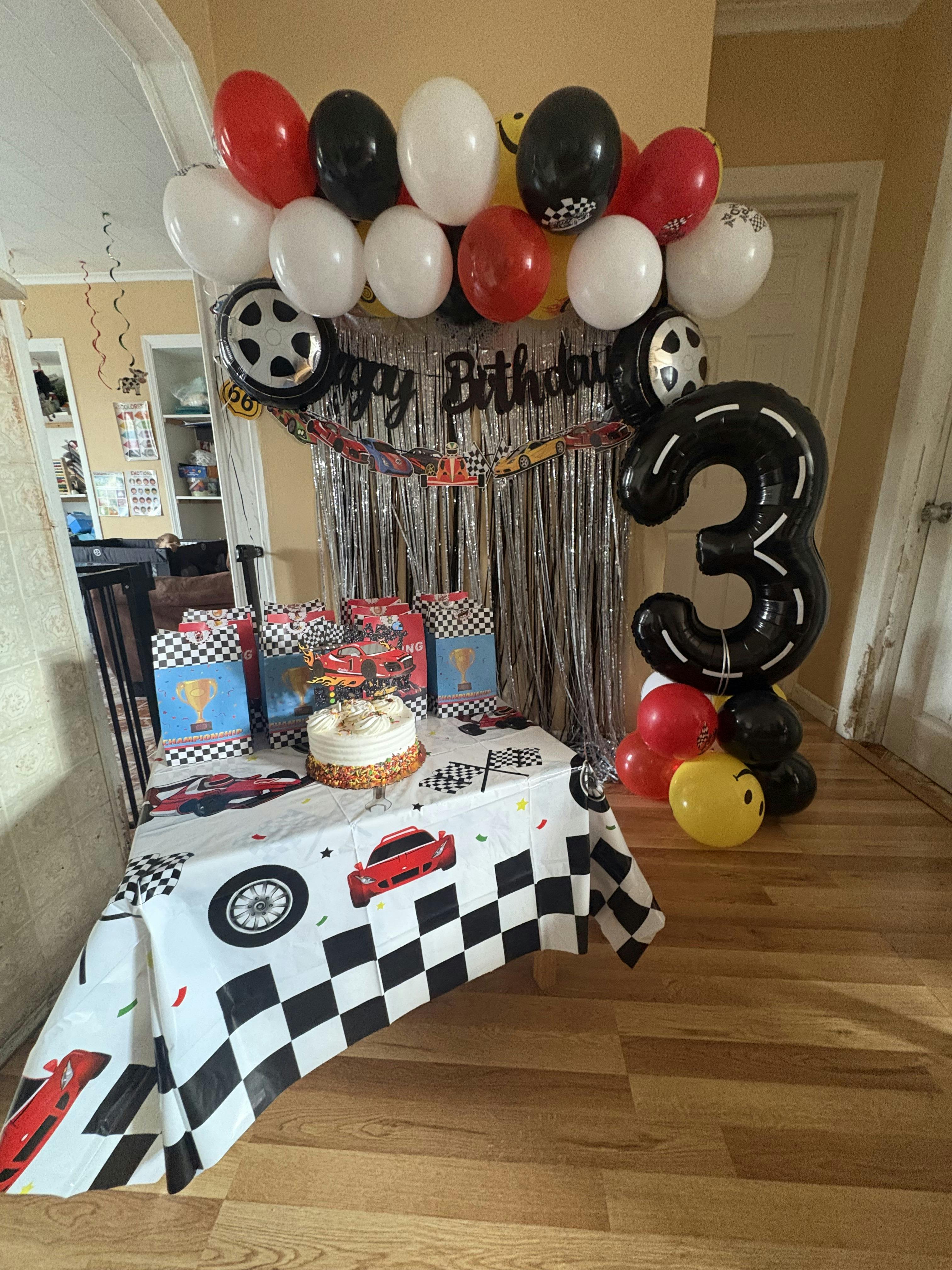 Birthday party decorations with a cake, gifts, and racing-themed balloons