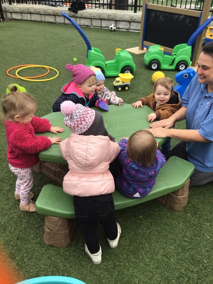 Adult and children gathered around a green picnic table outdoors
