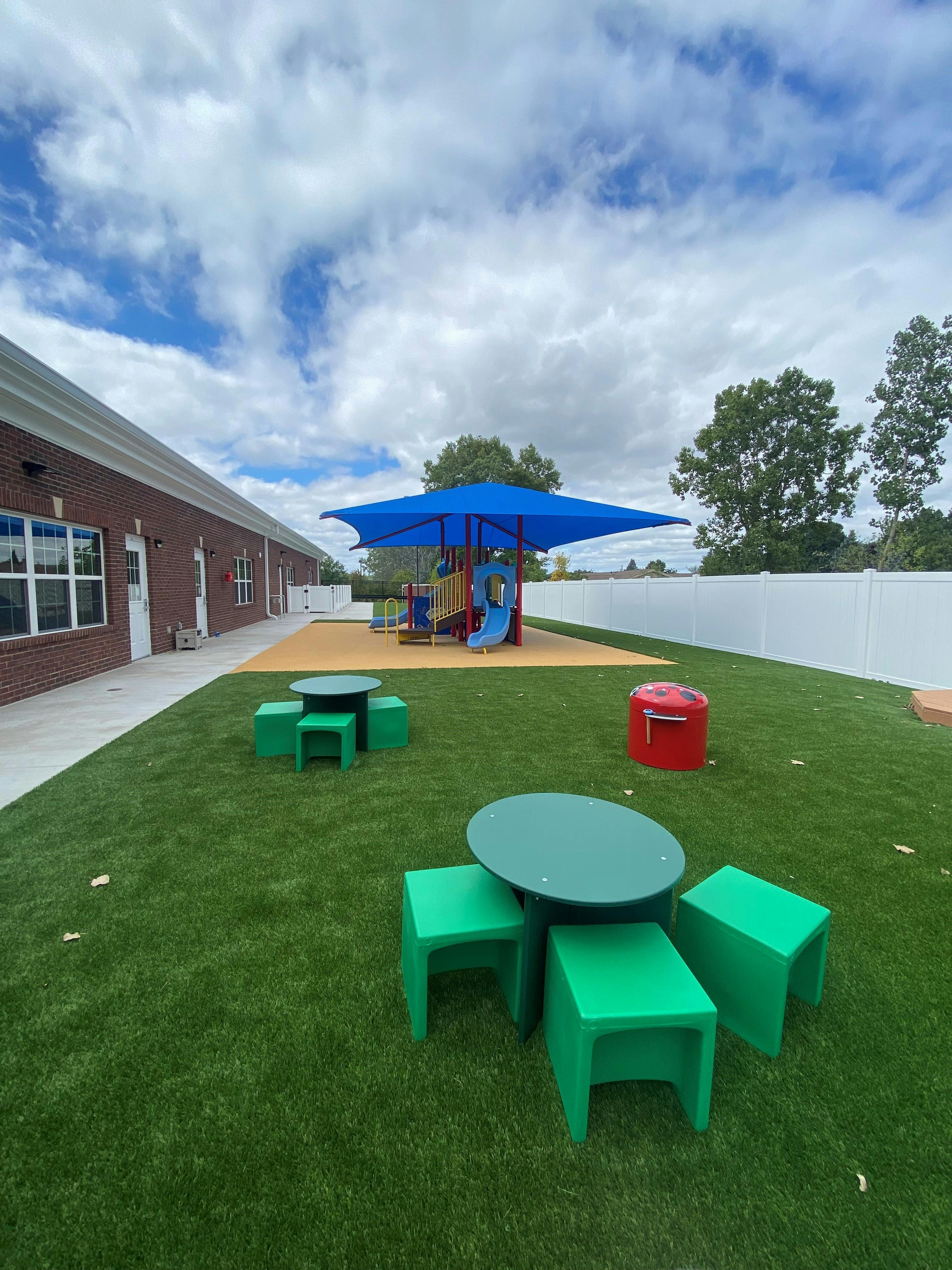 Outdoor playground area with green tables and stools on artificial grass