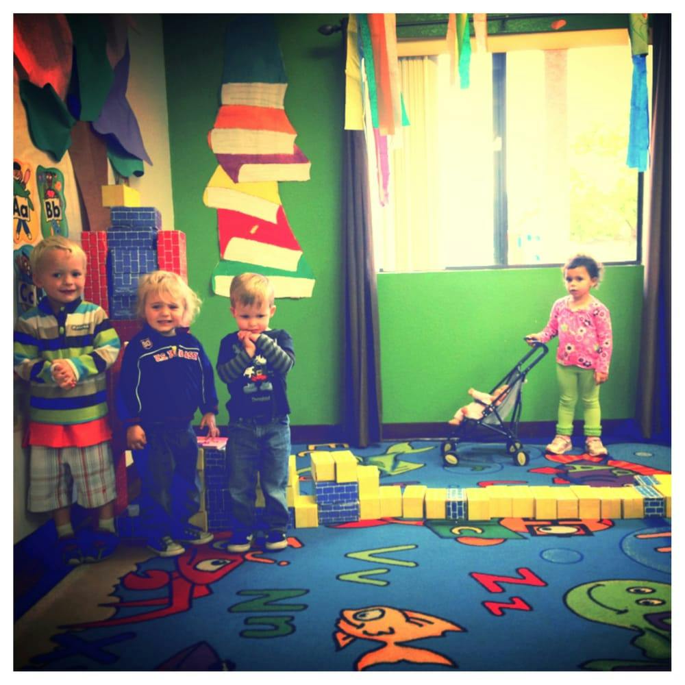 Four children in a classroom, one pushing a toy stroller