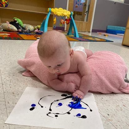 Child on a pink blanket making art with blue and black paint