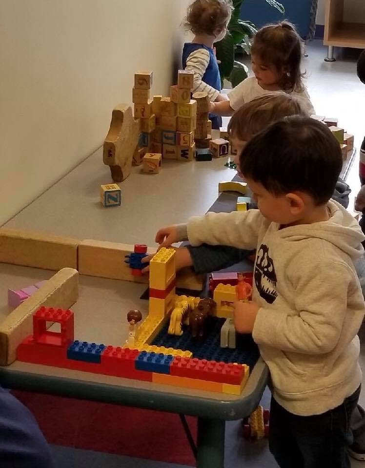 Children playing with building blocks and toy figures at a table