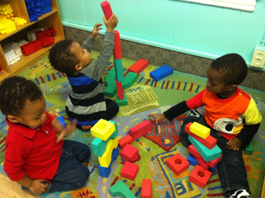 Three children playing with colorful building blocks on a rug