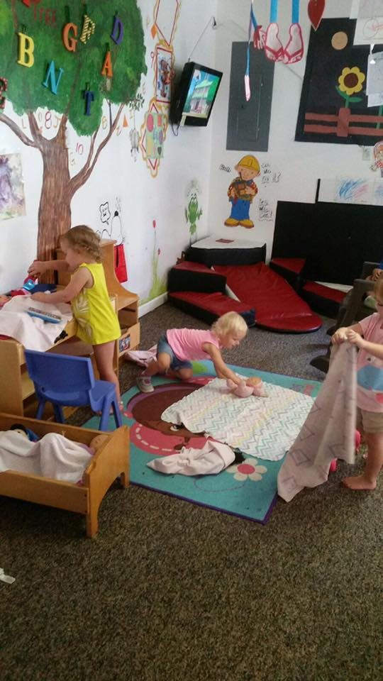 Three children playing with dolls and blankets in a room