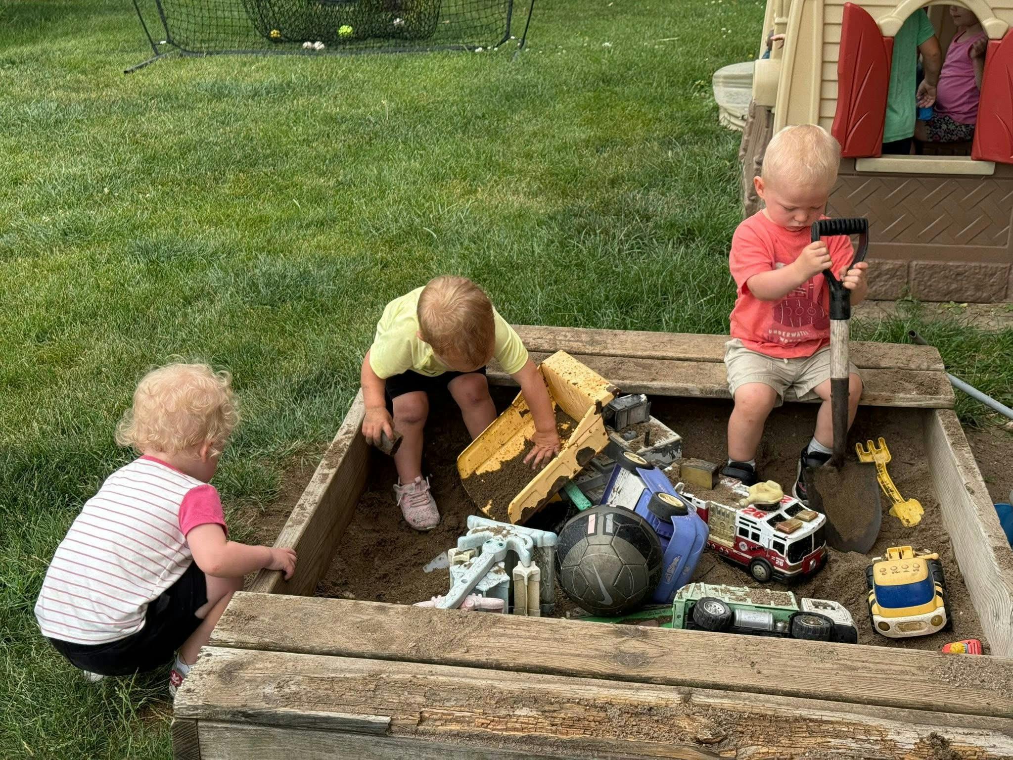 Three children playing in a sandbox with toys