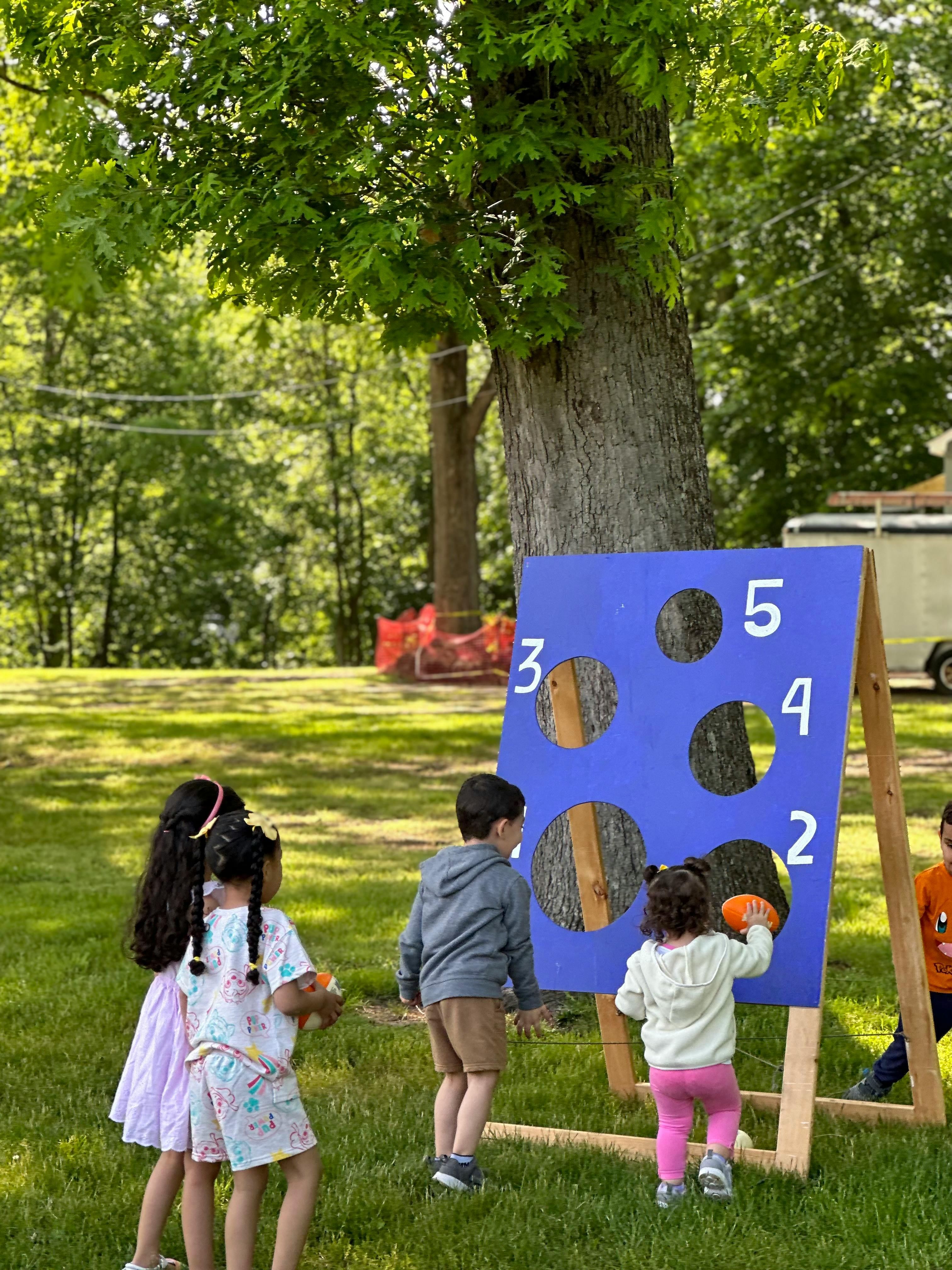 Children playing a beanbag toss game with a blue numbered board