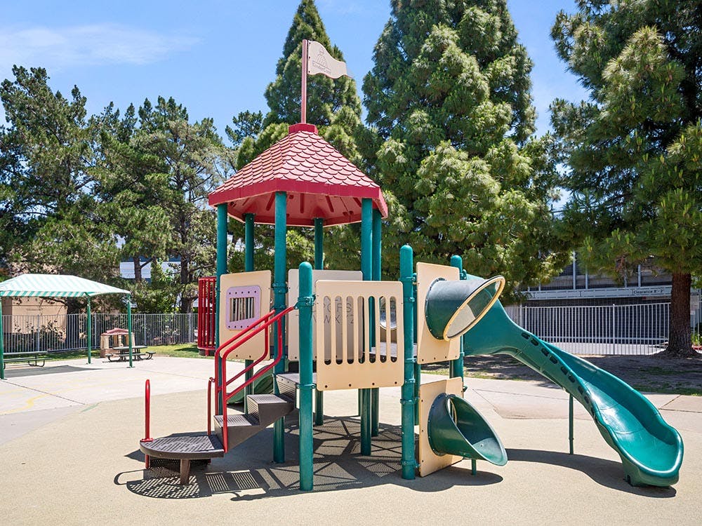Playground structure with a red roof, green slides, and steps