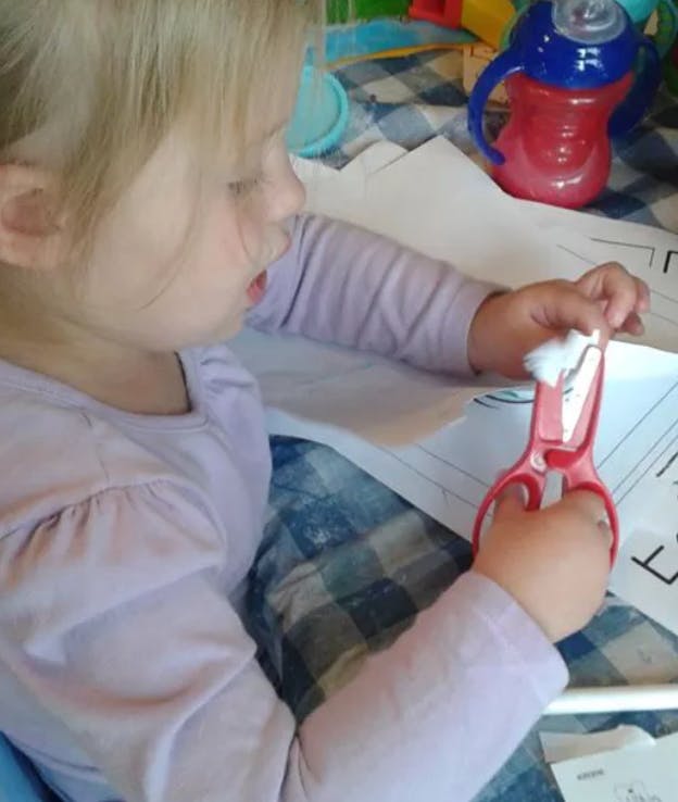 Child cutting paper with red scissors