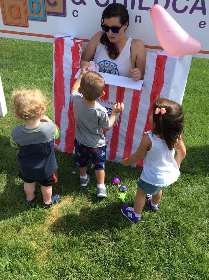 Person in sunglasses interacting with three children at a striped booth