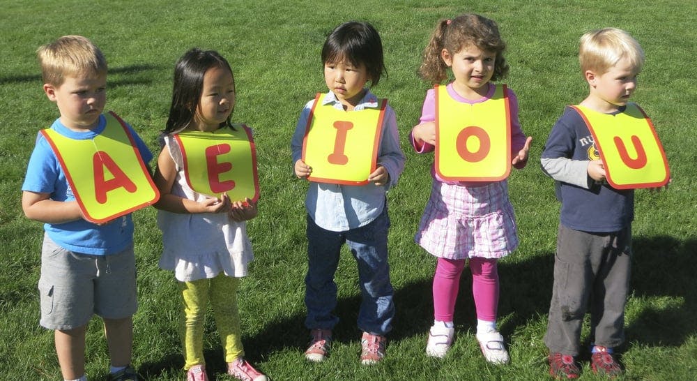 Five children holding signs with letters A, E, I, O, U