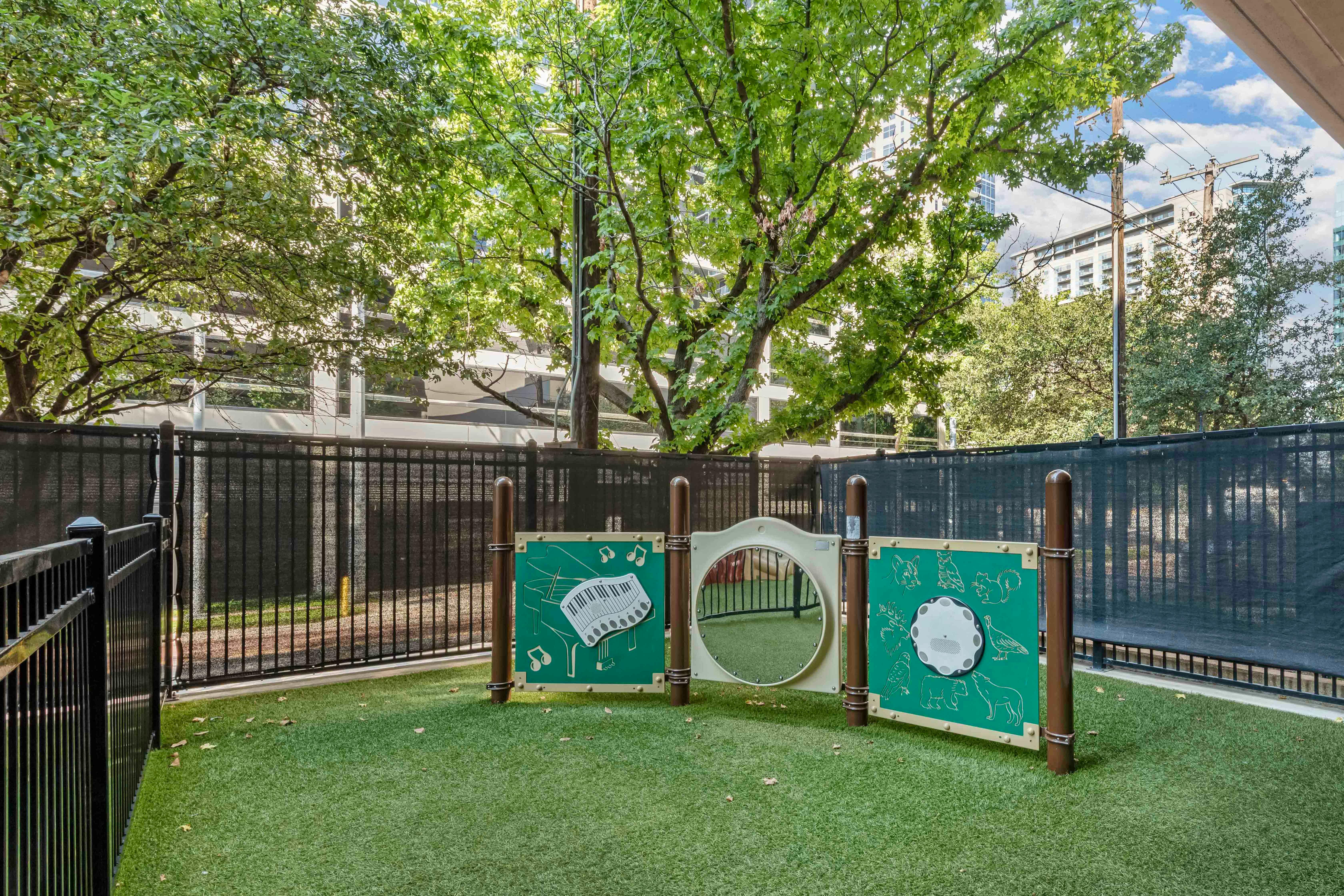A fenced-in outdoor area with artificial turf and children's play panels