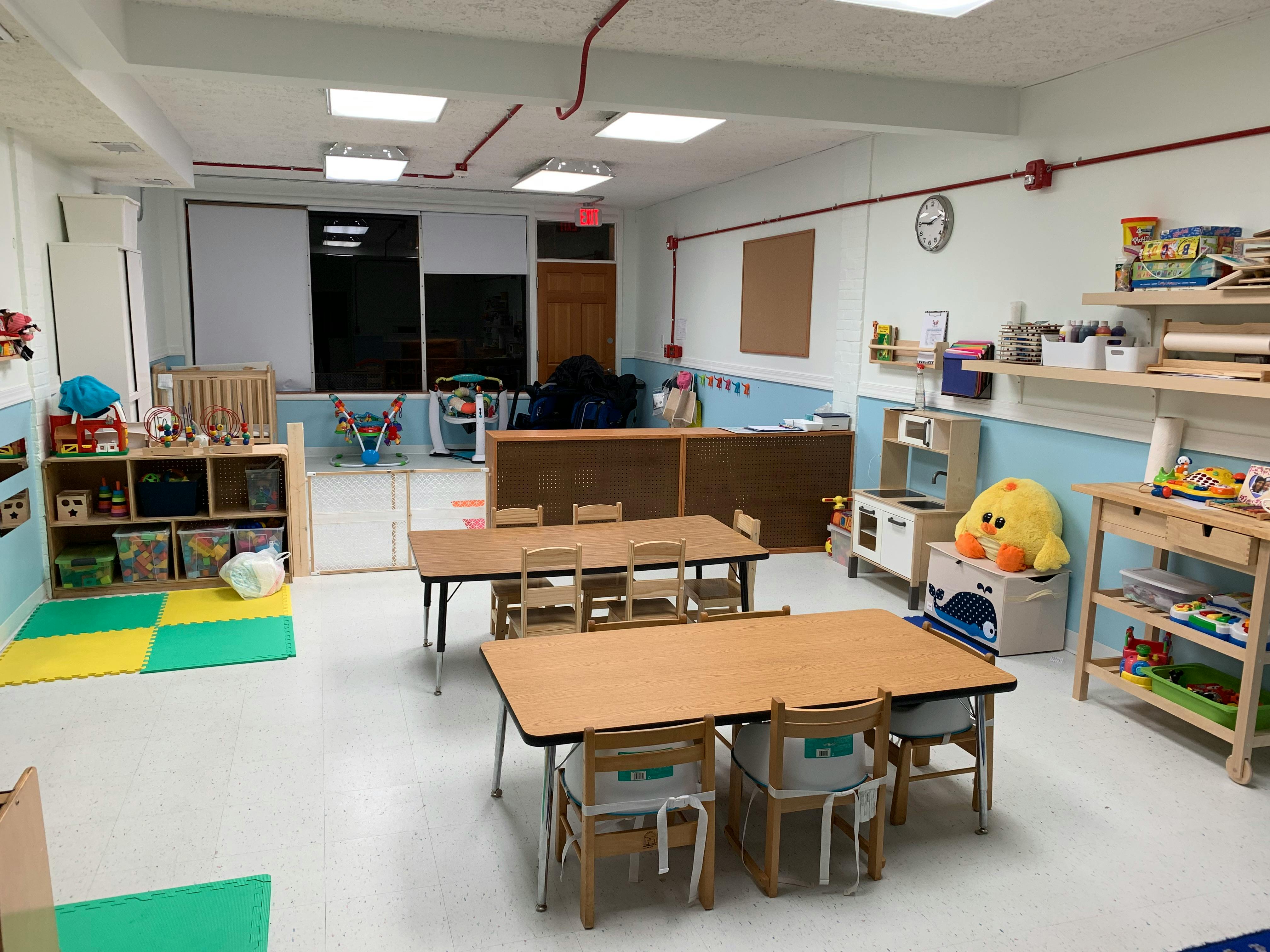 Classroom with small tables and chairs, shelves with toys, and a play kitchen