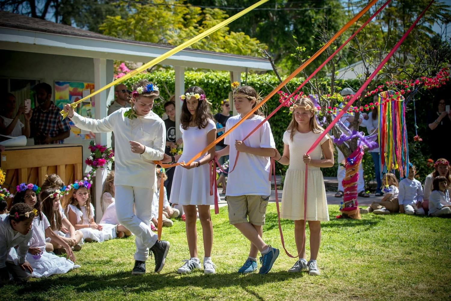 Group of children and teens dancing around a maypole with colorful ribbons