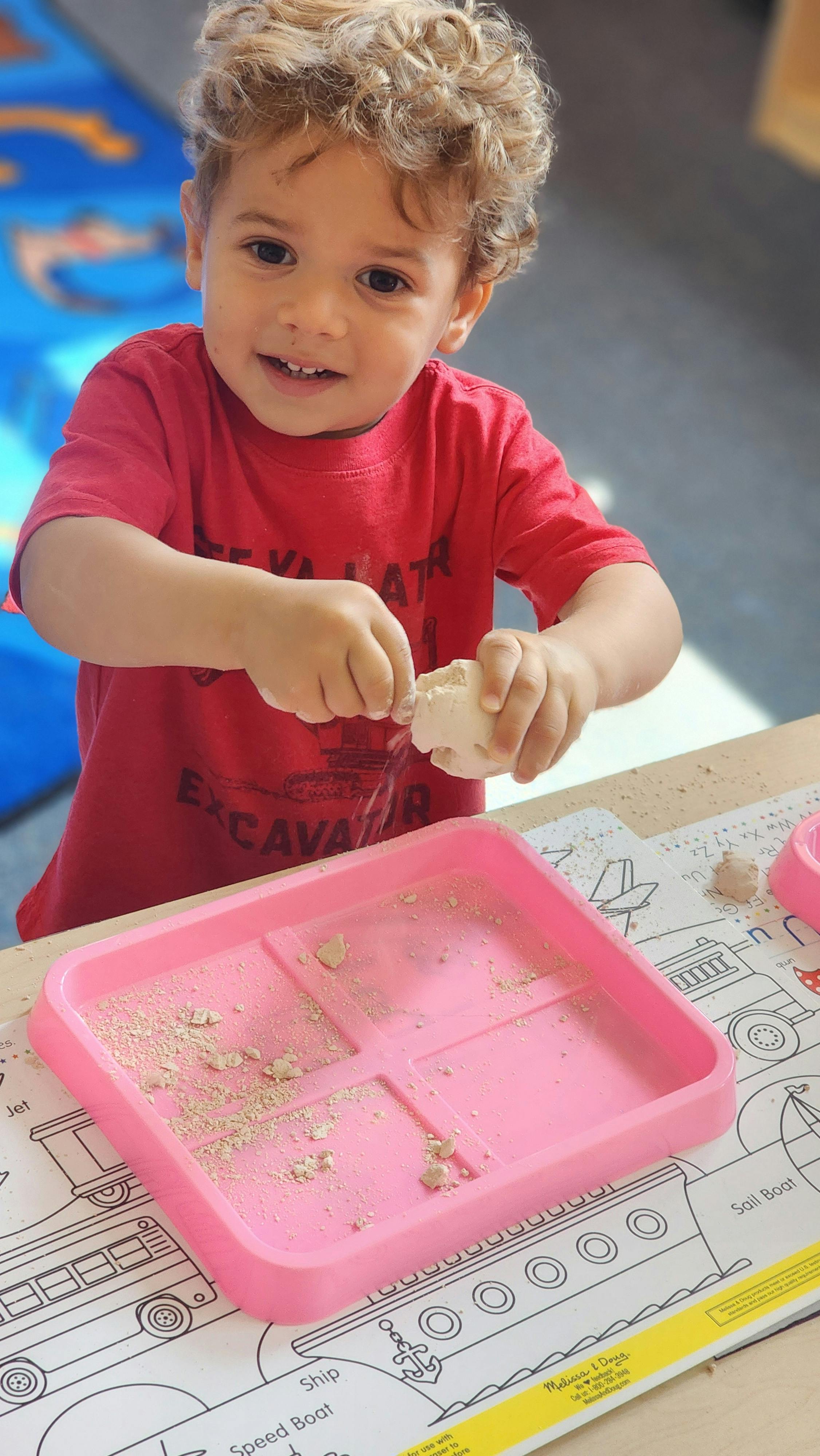 Child playing with sand in a pink tray