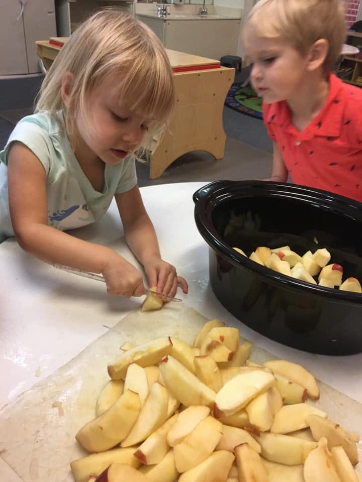 Child cutting apples with a knife, another child watching