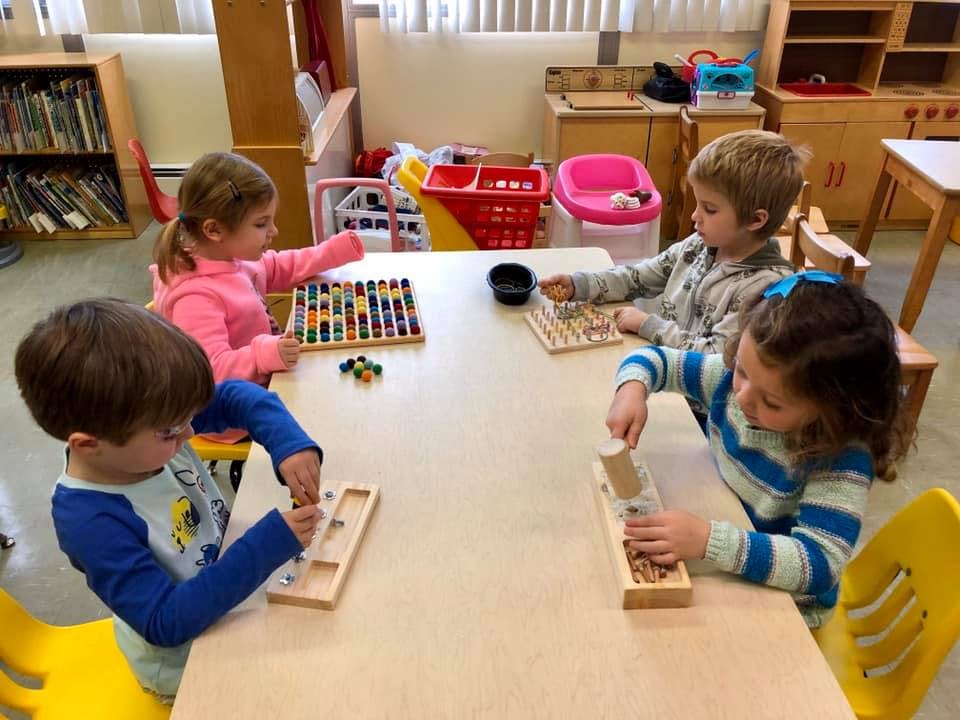 Four children playing with educational toys at a table in a classroom