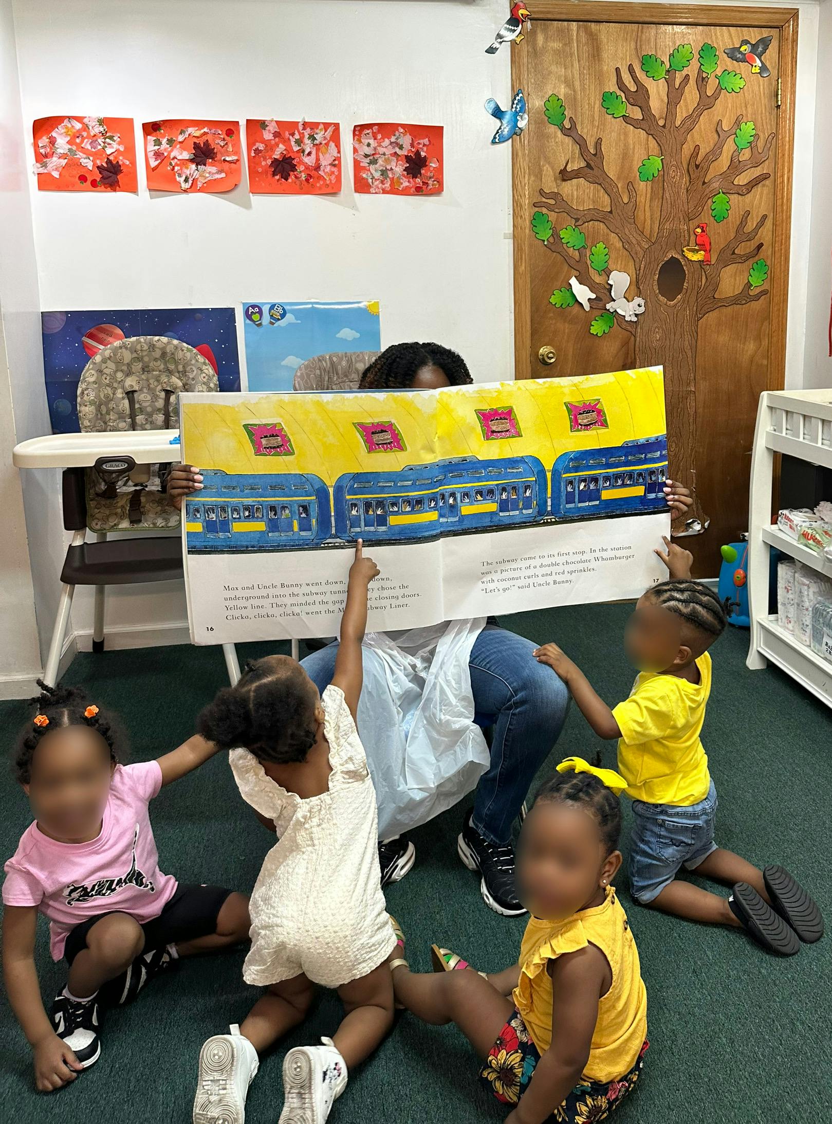 Adult reading a large book to three children pointing at illustrations of a subway