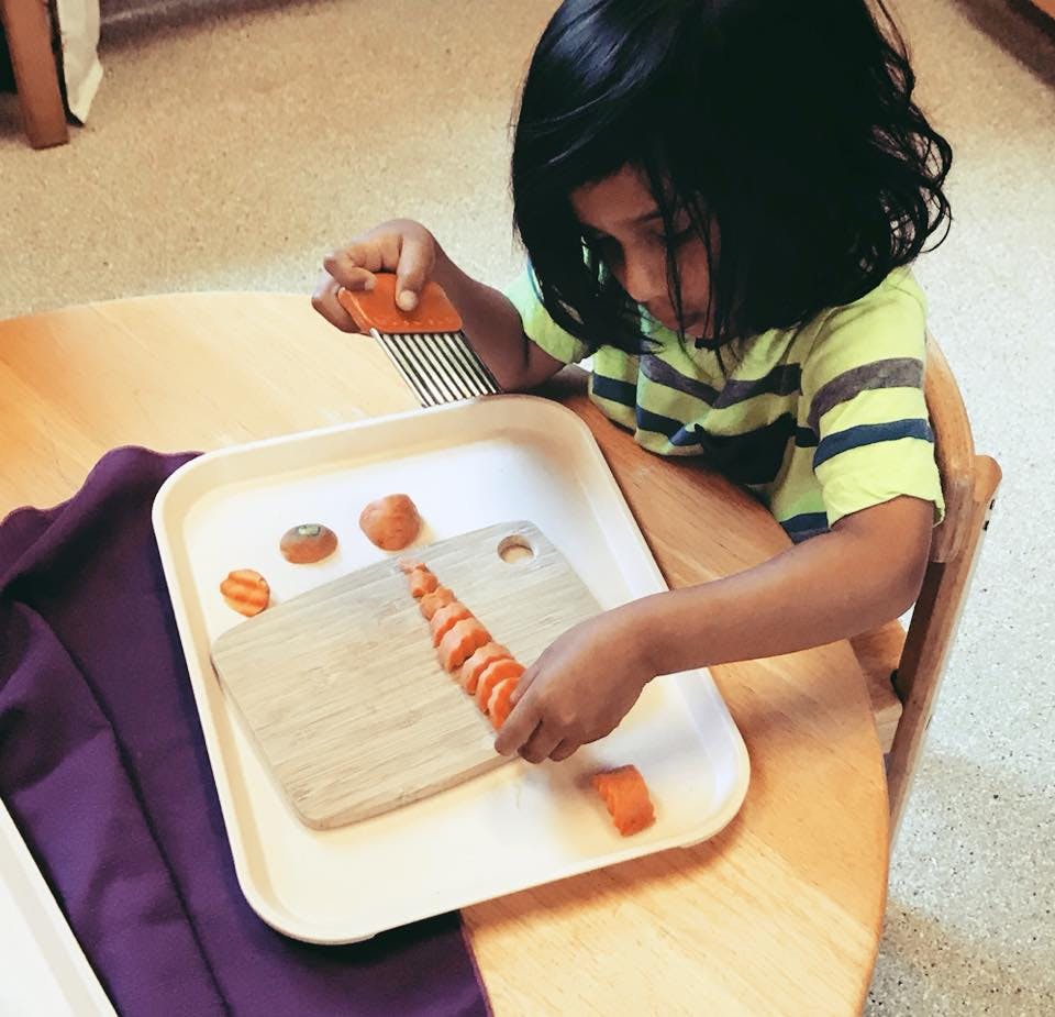Child cutting carrots on a tray with a crinkle cutter
