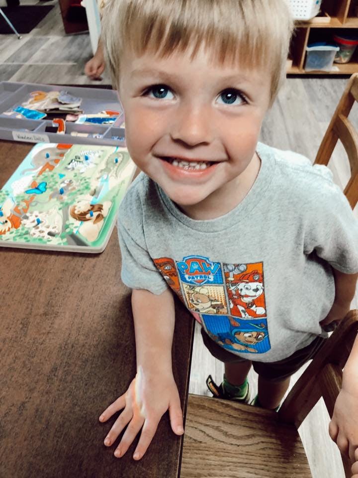 Child smiling at a table with puzzles