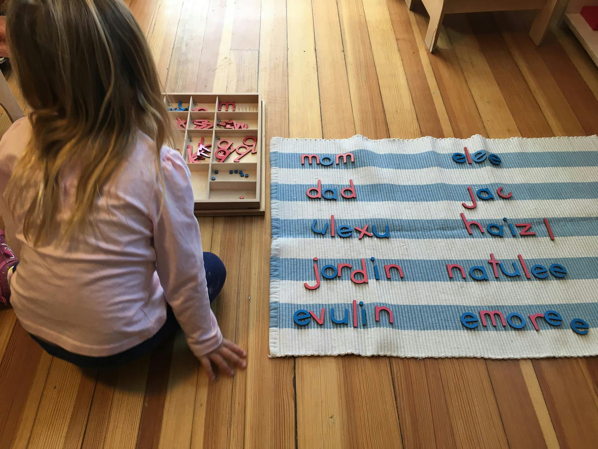 Child on floor next to a mat with letter tiles spelling words