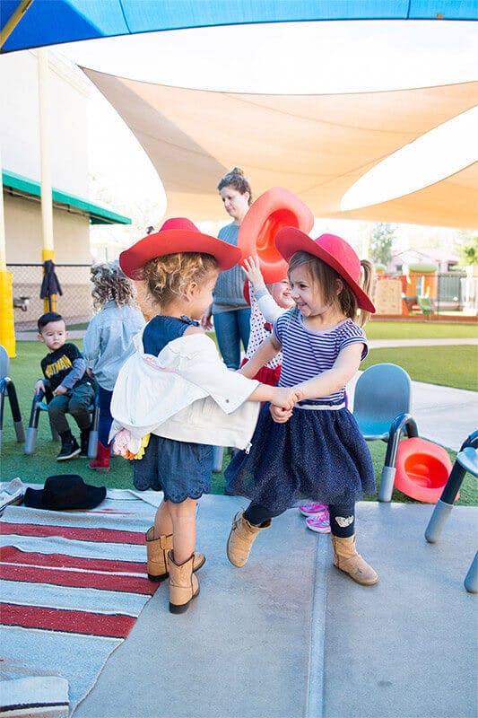 Two children in red hats holding hands and dancing outdoors